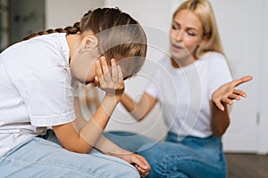 Close up side view of upset cute little girl crying covering face with palm while angry mother scolding at difficult