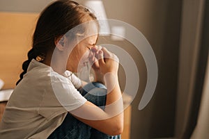 Close-up side view of upset little girl crying sitting alone on bed in bedroom. Concept of child depression.