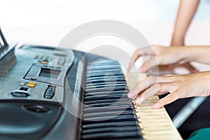 Close up side view of woman hands playing piano with hand of trainer blurry background.