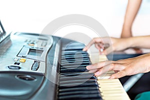 Close up side view of woman hands playing piano with hand of trainer blurry background.