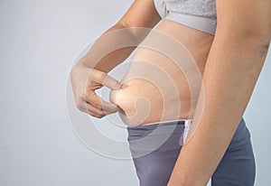 Close-up side view of woman`s hand pinching excessive belly fat  on gray background. Woman fat belly. Obesity and