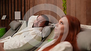 Close up side view of young couple lying on loungers poolside. Handsome bearded man flirting girl near pool with redhead
