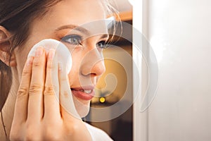 Close up side view of young woman removing make up off her face using a cotton pad and micellar water