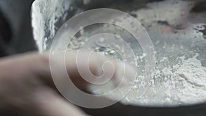 Close up of sieve sifting flour by old hands. Slow motion