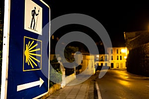 Close up of sign with arrow and yellow shell pointing the Camino de Santiago direction at night, which you need to follow to reach