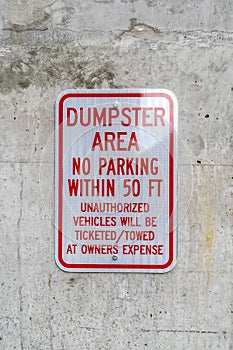 Close up of a sign that reads Dumpster Area No Parking against a concrete wall