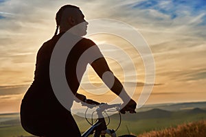 Close-up of silhouette of cyclist standing with bike against beautiful sunset.