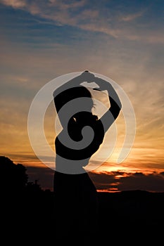 Close up silhouette of dancing woman at sunset. Image against the sun and orange sky