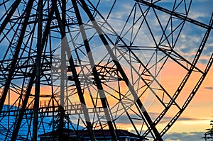 Close up silhouette of a part of ferris wheel without cabins on the blue and orange cloudy sky backgorund against the