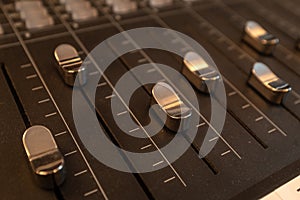 A close up of silver-coloured sliders on a mixing desk in a music studio