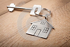 Close up silver home shaped keychain with key on wooden background. Mortgage, investment, real estate, property and new home conce