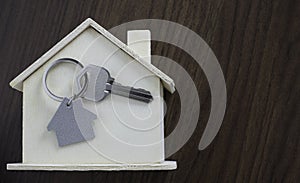 Close-up of Silver key house with house shaped keychain and home mock-up on wooden table background.