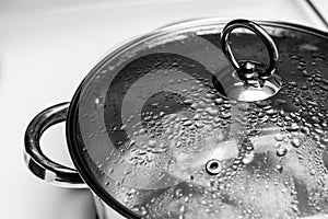 Close up of a silver metal pot with lid on circular handle on top with condensation boiling water isolated on white background