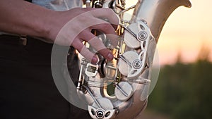 Close up silver sax play by bearded musician in gray shirt performs his part on beautiful shiny saxophone at sunset or