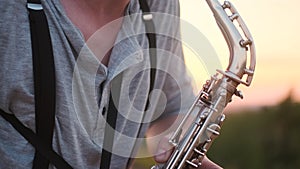 Close up silver sax play by musician in gray shirt performs his part on beautiful shiny saxophone at sunset or sunrise