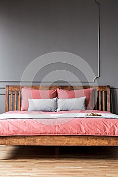 Close-up of a simple bed with wooden bedhead and pink sheets in