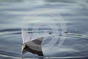 Close-up of simple small white origami paper boat floating quietly in blue clear river or sea water under bright summer sky. Freed