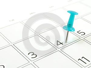 close-up single blue plastic pushpin tacking in 4th of july on schedule grid of desk calendar page