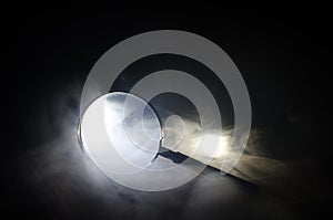 Close up Single Magnifying Glass with Black Handle, Leaning on the Wooden Table on orange red smoke dark background. Surreal backg