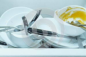 Close-up of sink full of dirty white tableware, plates, bowls, knives, forks, spoons. Cooking, housekeeping, cleaning.