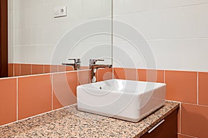 Close-up of sink with a mirror and red tiles in new compact bathroom after renovation. Concept of a beautiful stylish