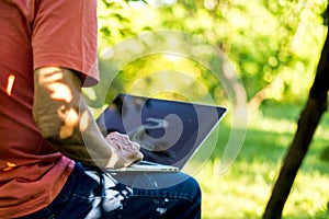 Close up sitting senior retired freelancer working on laptop on a summer resort