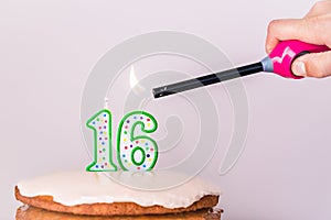 Man`s hand lighting sixteenth birthday candles on rustic vanilla layer cake photo