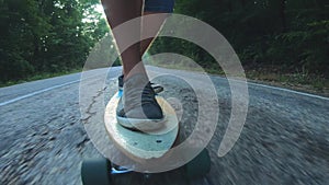 Close-up skateboarder boy riding outdoor. A young man rides a longboard on the highway. Misty road in the forest