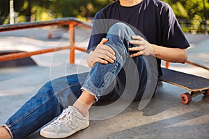 Close up skater holding his painful leg with skateboard near at skatepark isolated