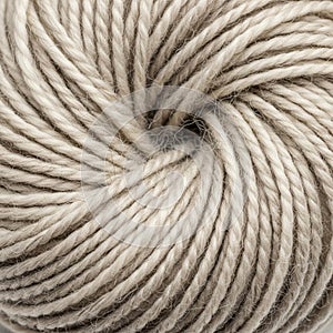 Close-up of a skein of yarn tightly wound in a circular pattern. The yarn is beige, with a