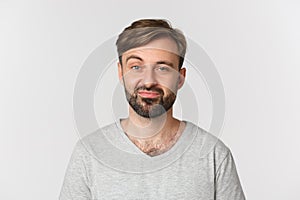 Close-up of skeptical and unamused bearded man, wearing gray t-shirt, standing over white background