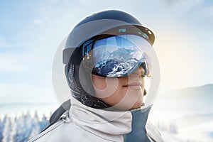 Close Up Of The Ski Goggles Of A Man With The Reflection Of Snowed Mountains. Man In The Background Blue Sky.