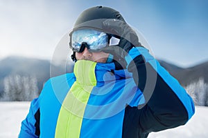 Close Up Of The Ski Goggles Of A Man With The Reflection Of Snowed Mountains. Man In The Background Blue Sky.