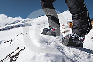 A close-up of a skier`s leg in ski boots without skis stands on a knoll of bliss against the background of mountains on