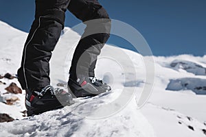 A close-up of a skier`s leg in ski boots without skis stands on a knoll of bliss against the background of mountains on