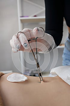 Close up of skin held in piercing tool as needle is ready to go in to pierce naval.