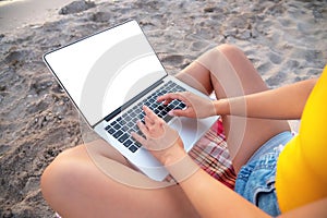 Close-up of a slender young woman on the beach at the sunset time by the sea works on her laptop holding him on her lap