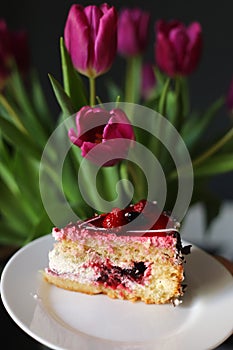Close up of slice of berry cake on a white plate near beautiful tulips flowers. holiday. birthday cake