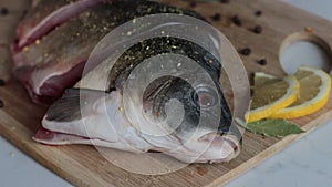 Close up of sliced carp fish on cutting board. Spices dropping onto raw fish. Female hand lays pieces of lemon over fillet