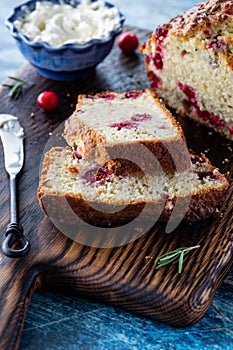 Close up of a sliced cranberry rosemary quick bread with cream cheese topping in behind.