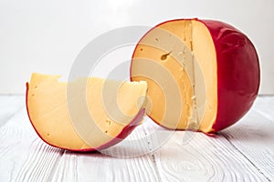 Close up. Sliced piece of cheese Edam and dutch head of cheese on white wooden background