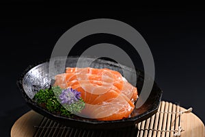 Close up sliced salmon sashimi serve on black plate with parsley leaf. Japanese food style