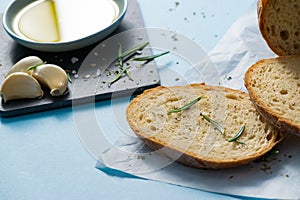 Close up slices of bread with Rosemarie and saucer with olive oil on papyrine on blue background