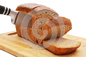 close-up of slicing loaf of rye bread with knife on cutting board on white background
