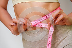 Close up of slim woman measuring her waist& x27;s size with tape measure. Isolated on white background.