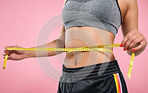 Close up of slim woman measuring her waist`s size with tape measure on pink