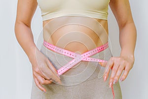 Close up of slim woman measuring her waist& x27;s size with tape measure. Isolated on white background.