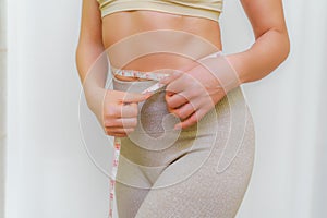Close up of slim woman measuring her waist& x27;s size with tape measure. Isolated on white background.