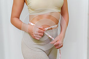 Close up of slim woman measuring her waist& x27;s size with tape measure.  on white background.