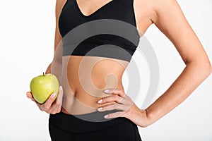 Close up of slim women`s body in sportswear holding apple
